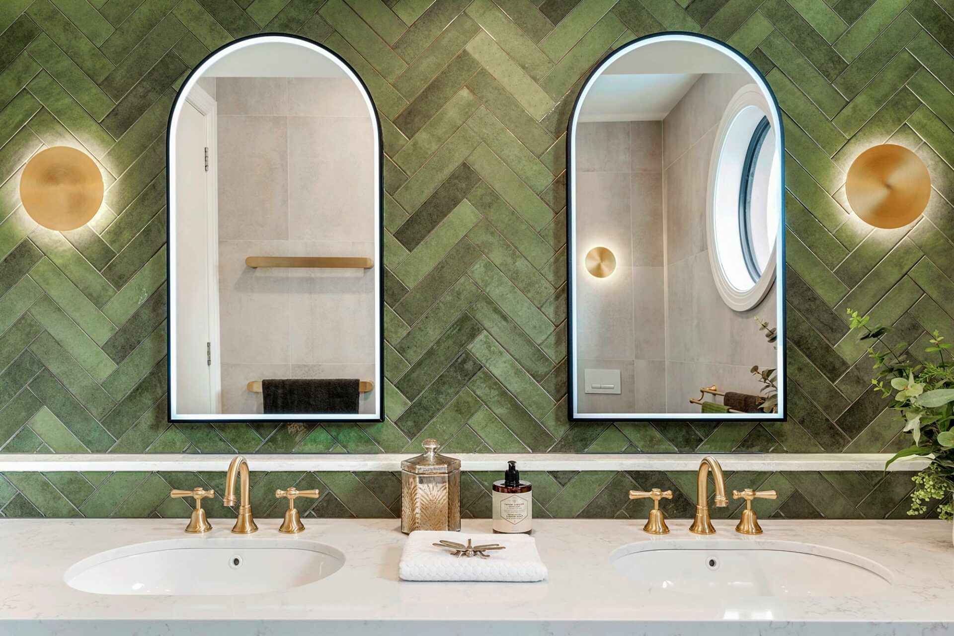 Twin ensuite bathroom, showcasing twin basins and arch mirrors againse green wall tiles